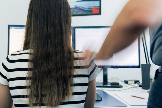 Eine Frau, welche am Computer sitzt, wird von einem Mann ungewollt angefasst. 