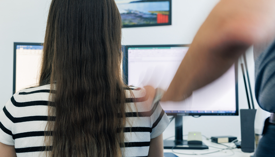 Eine Frau, welche am Computer sitzt, wird von einem Mann ungewollt angefasst. 